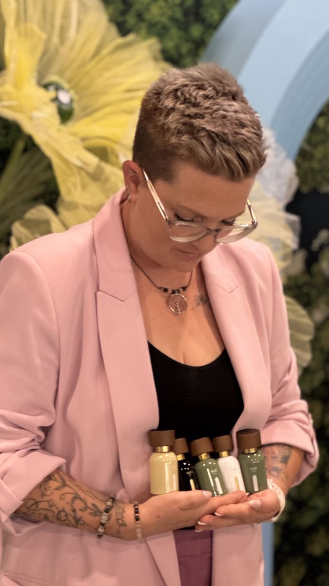Sabrina im rosa Blazer mit fünf Wyld-Notes-Parfumflaschen in den Händen