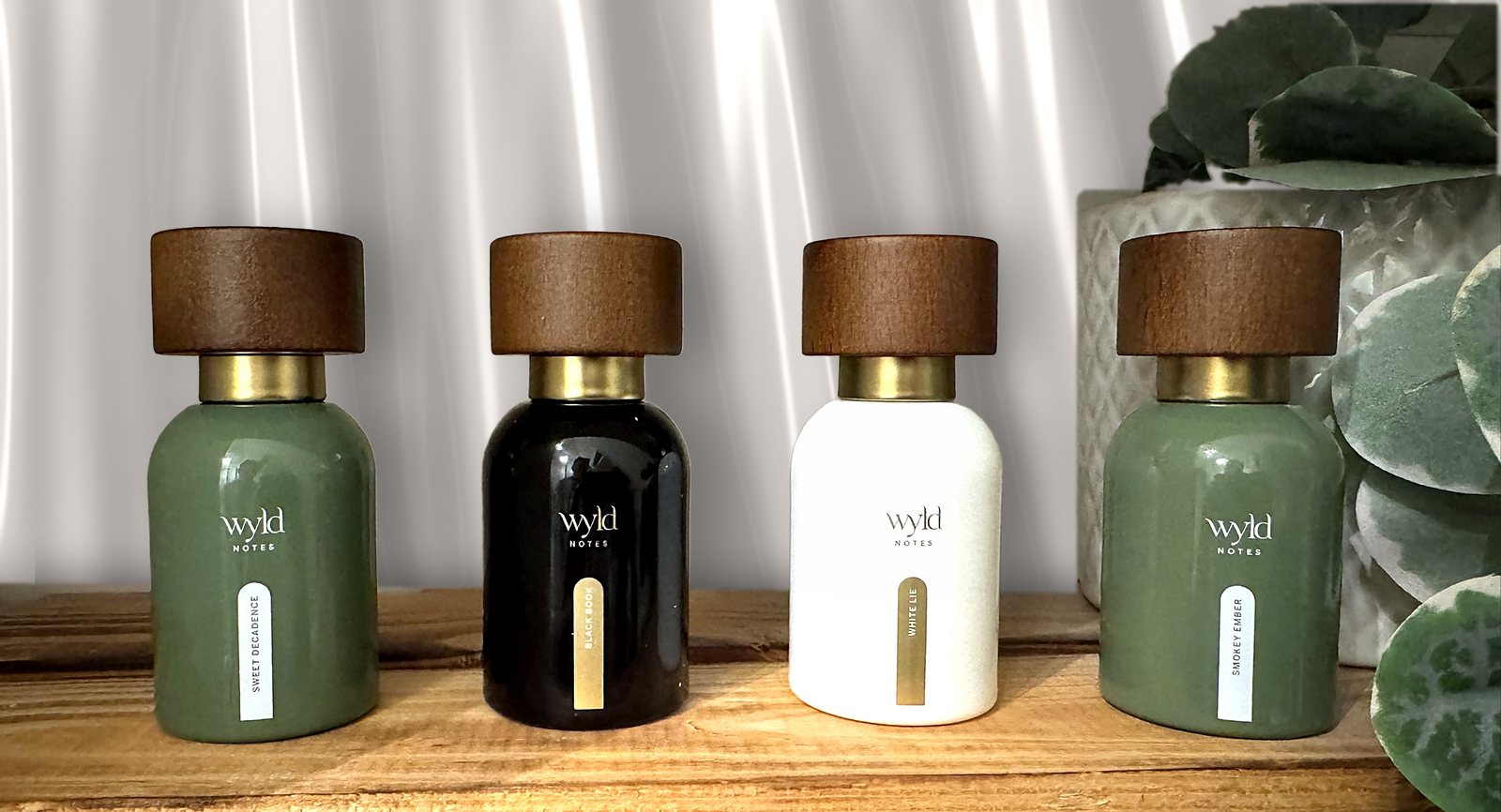 Vier Wyld-Notes-Parfumflaschen auf einem Holzregal vor einem weißen Satinvorhang