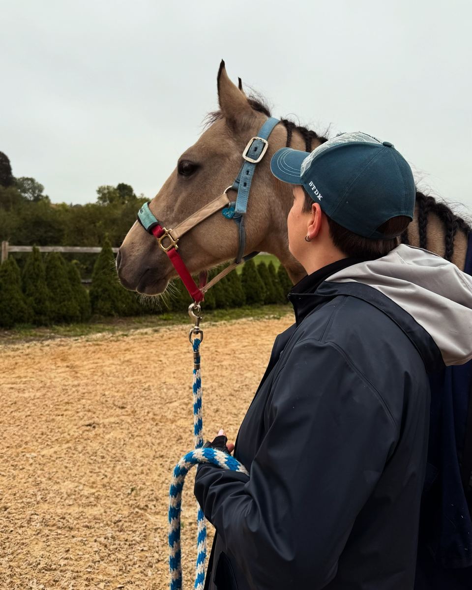 Sabrina mit Cap steht neben einem Pferd auf dem Reitplatz